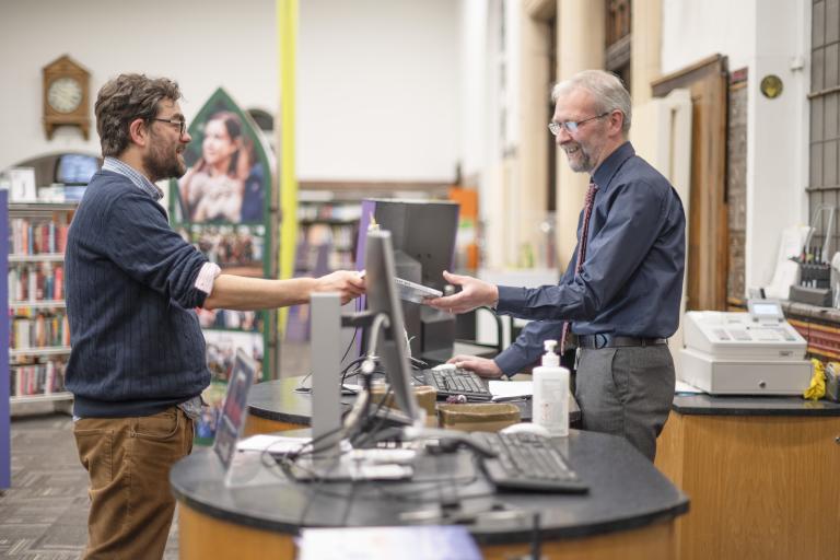 Librarian passing book to a patron in a library