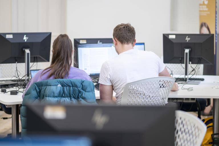 Two people working at a computer, viewed from behind