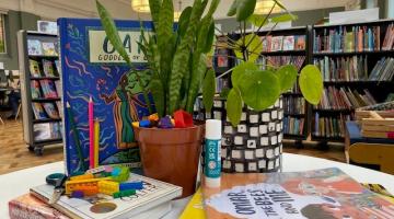 A photo of books and plants on a table, with book shelves in the background