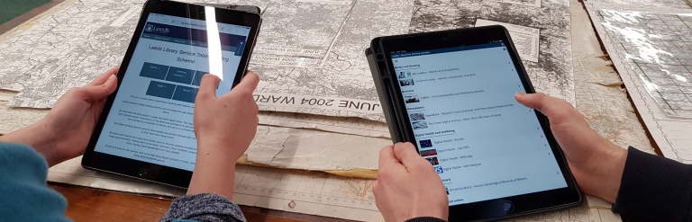 two people looking at ipads while sat at a table with maps on it.